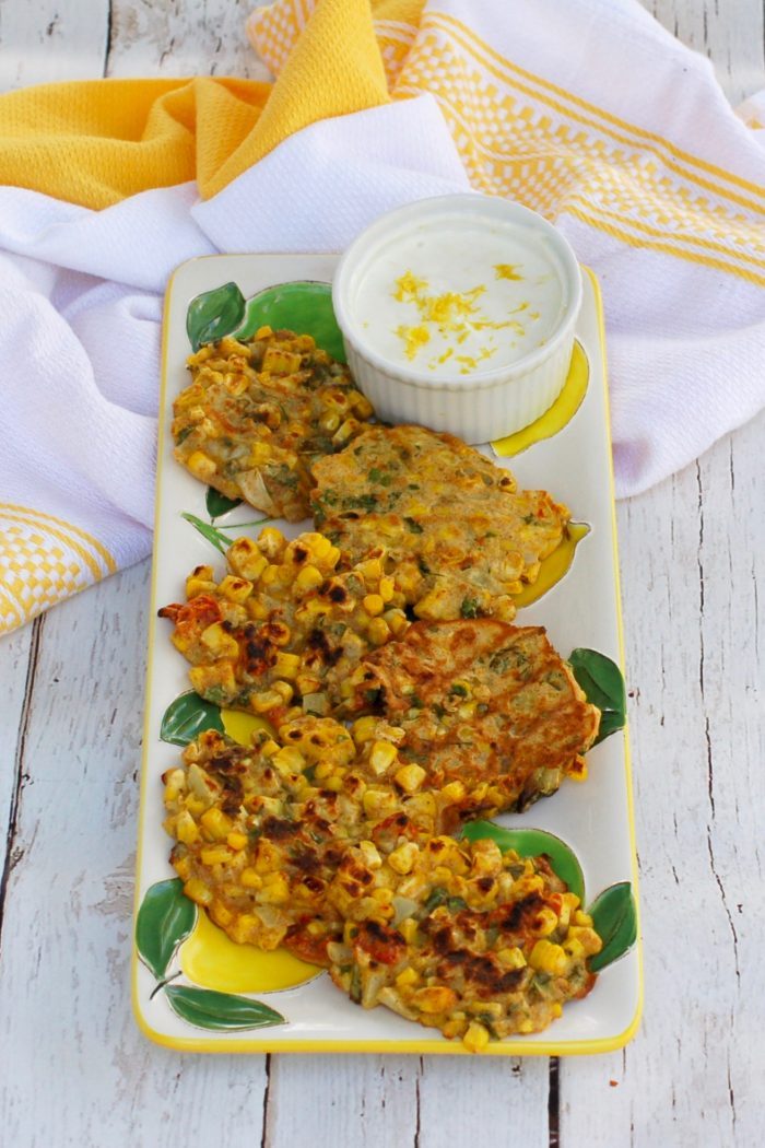 overhead picture of Corn & Basil Cakes on serving plate with ramekin of yogurt sauce