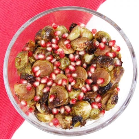 roasted brussels sprouts with pomegranate seeds in glass serving bowl