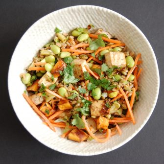Asian-Style Farro Buddha Bowl with Crispy Baked Tofu | Whole grain farro is topped with shredded carrots, edamame, roasted Brussels sprouts and sweet potatoes, and crispy baked tofu and then tossed with a miso lime dressing for a vegetarian and vegan-friendly meal the whole family will love. Get the recipe at JessicaLevinson.com | #meatlessmonday #farro #buddhabowl #vegetarian #dairyfree #eggfree #healthyrecipe #weeknightdinner #dinnerrecipe #lunchrecipe #tofu