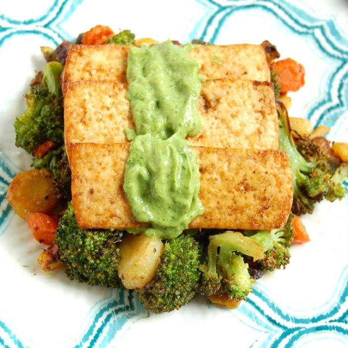 Close Up of broiled tofu over roasted broccoli, carrots, and parsnips topped with avocado sauce