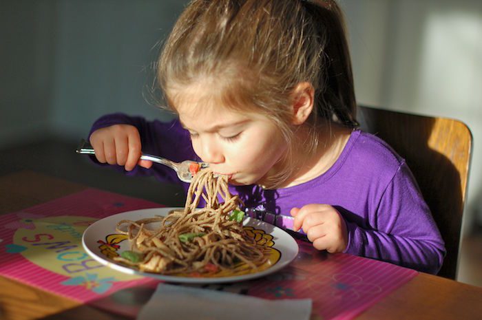 little girl eating noodles with vegetables