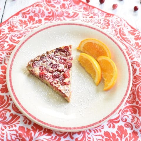 slice of cranberry dutch baby on plate with sliced oranges
