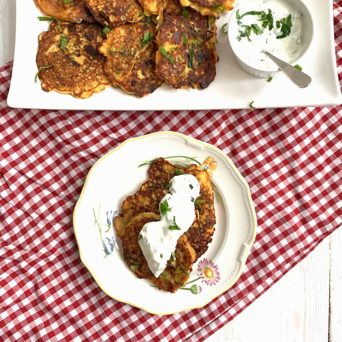 gluten free zucchini pancakes stacked on plate with yogurt sauce on top and serving platter in background