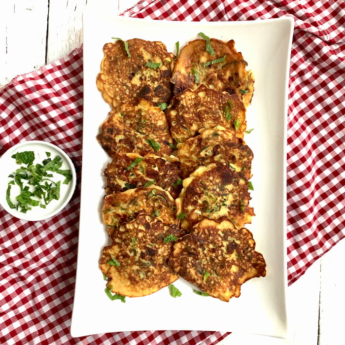 zucchini pancakes on white serving platter with side ramekin of yogurt sauce