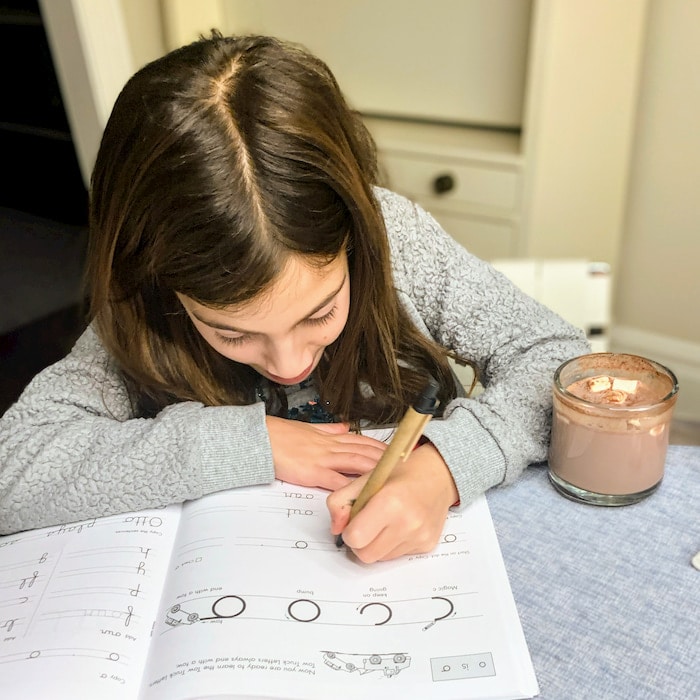 young girl doing homework with a cup of hot chocolate