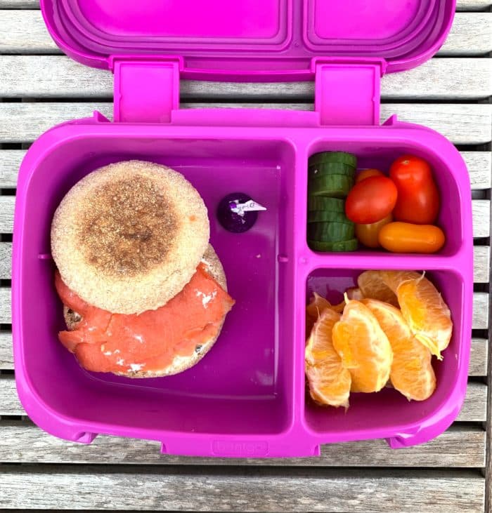 bento box lunchbox with english muffin and smoked salmon, orange segments, cucumbers and tomatoes
